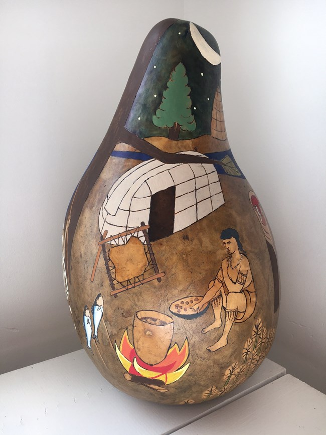 Gourd painted with a scene of a woman cooking next to a fire with pottery and a longhouse