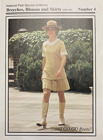 A woman wearing a tan dress, tan hat and tan knee boots walks towards us.