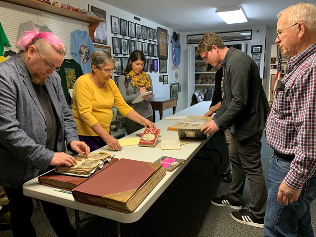 Six people standing around a long table examining part of a museum collection