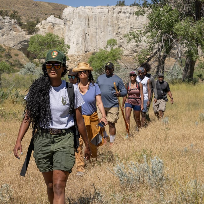 A group hiking through a field near cliffs