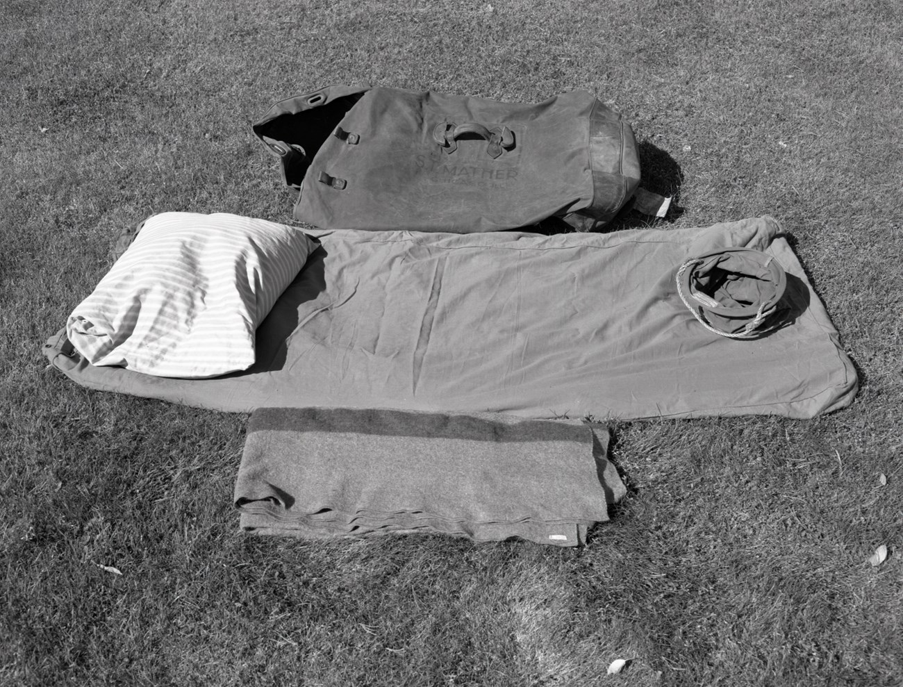 Mather's camping gear Deflated mattress, blanket, pillow, bag, and bucket on ground