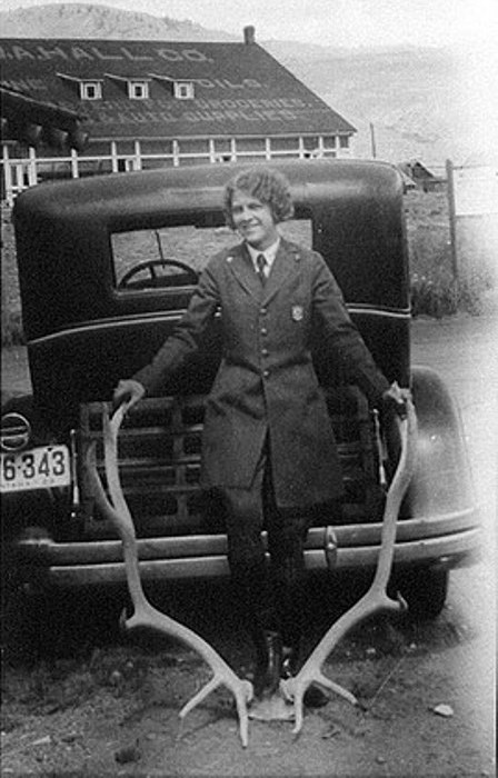 Ranger Frances Eva Pound in her Park Service uniform stands in front of a car, holding onto large antlers.