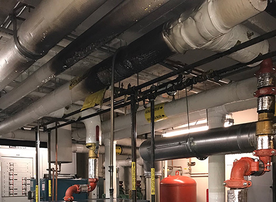 Scorched pipe insulation Inside a boiler room with scorched pipes overhead.