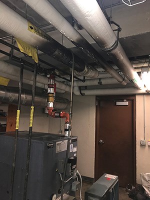 Interior of a boiler room with pipes covered in soot running across the ceiling.