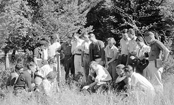 YOSE field school_1937 Men and women sitting in a field look towards a man in the middle