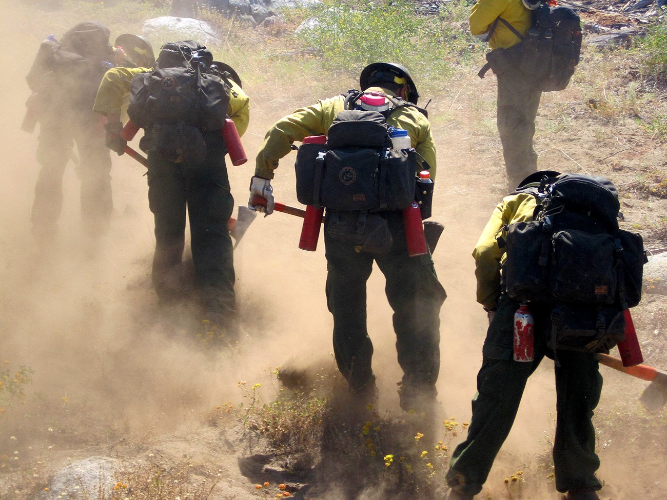 firefighters in full gear digging a line in a dusty environment.