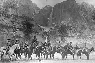 Nine people sit on horses with a waterfall in the back middle of the frame.