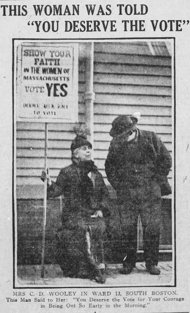 YouDeservetheVote_BG_Nov2_1915 woman sitting holding a sign while a man leans over to talk to her