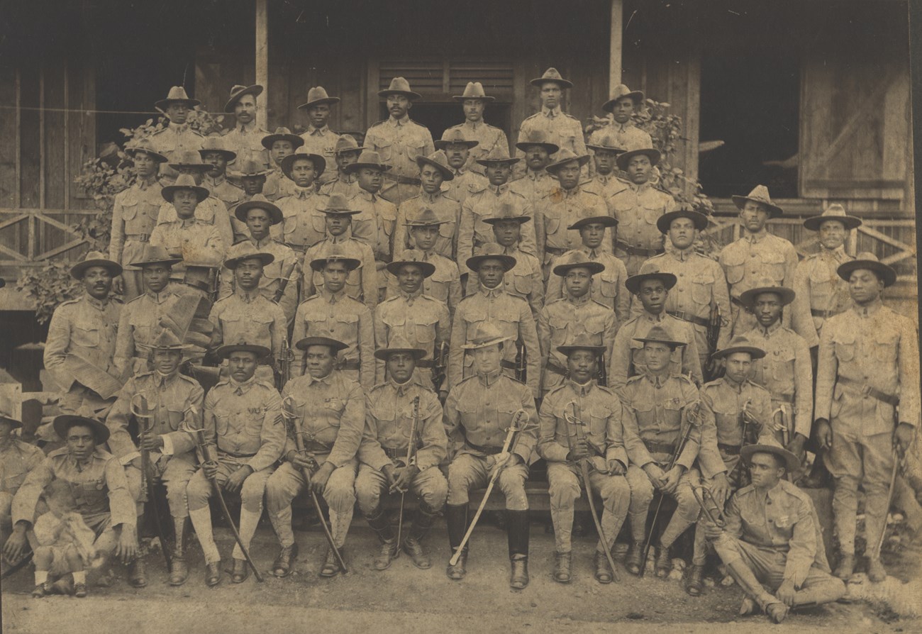 Historic black and white photo of a few lines of Buffalo Soldiers seated for a group picture