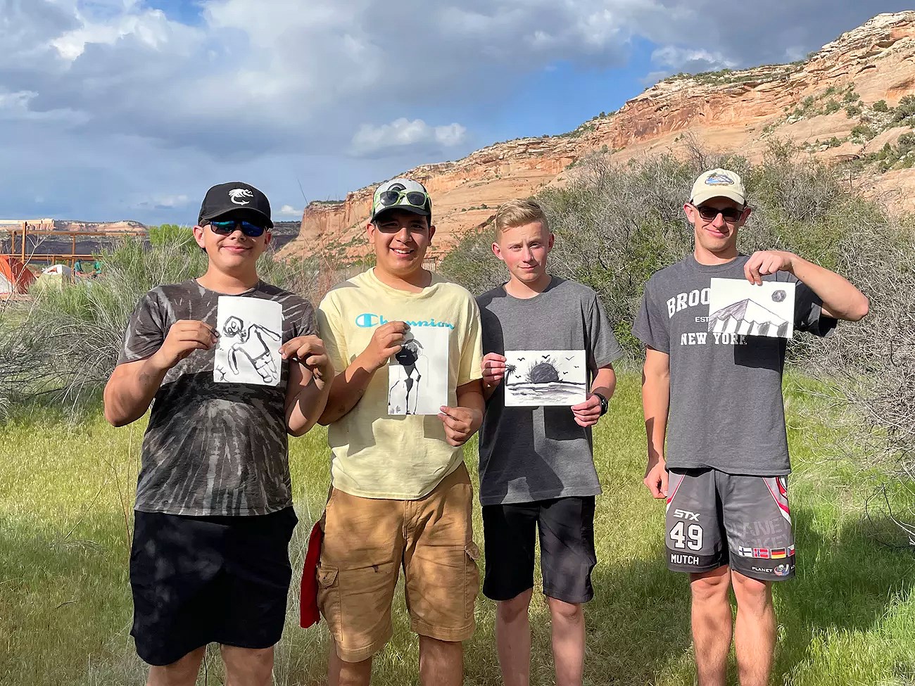 Four students outside holding up sketches of outdoor subjects