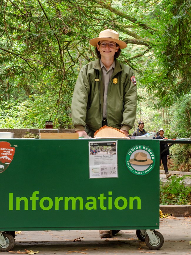 Ranger in uniform behind a wheeled table along a trail in the heart of Muir Woods.