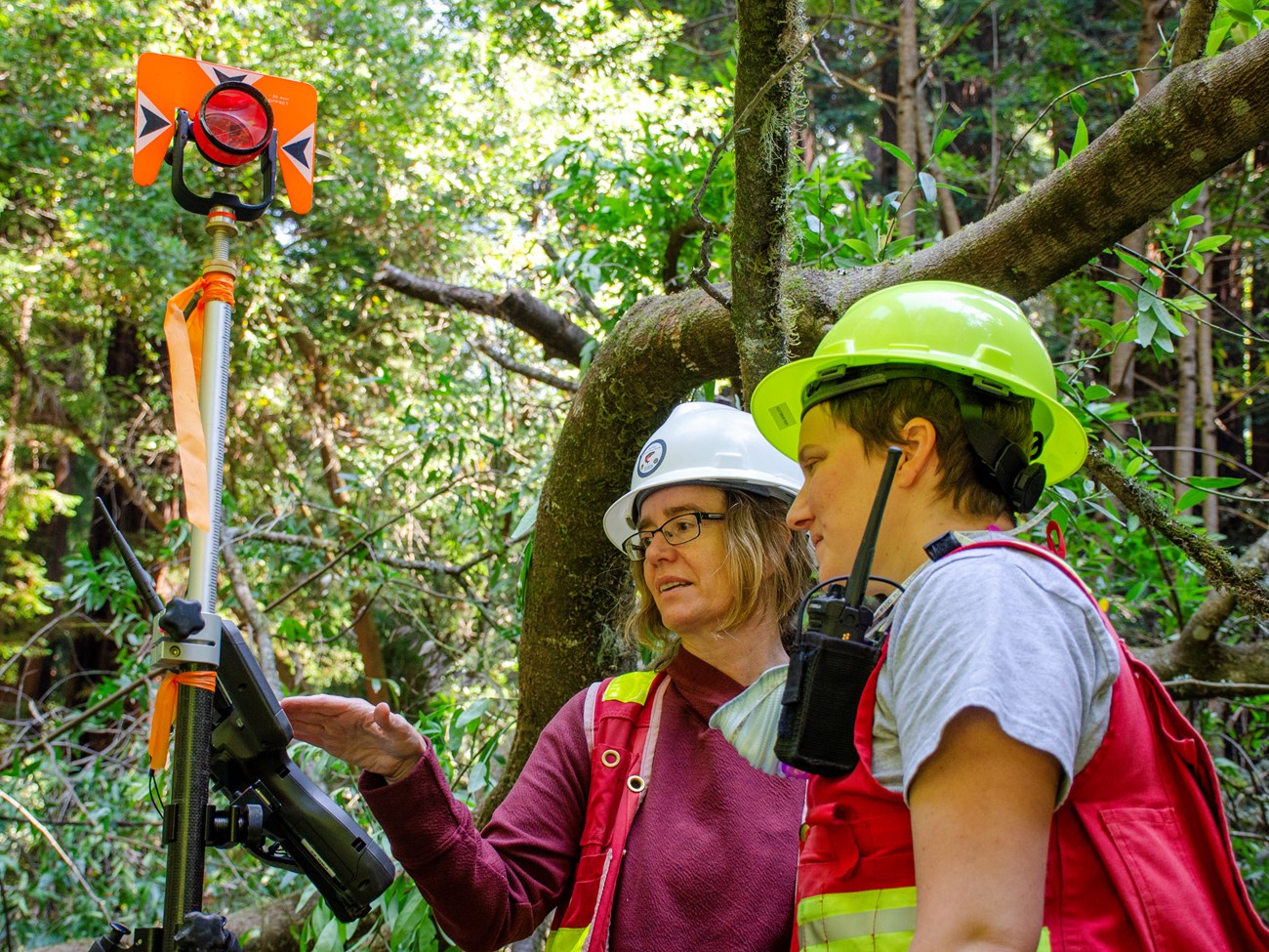 Two people in safety vests and hard hats focused on a piece of site survey equpment at the restoration site.