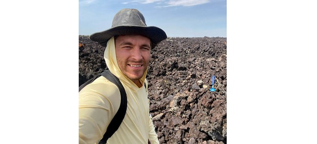 man in hat and yellow sun shirt standing in front of rocky landscape