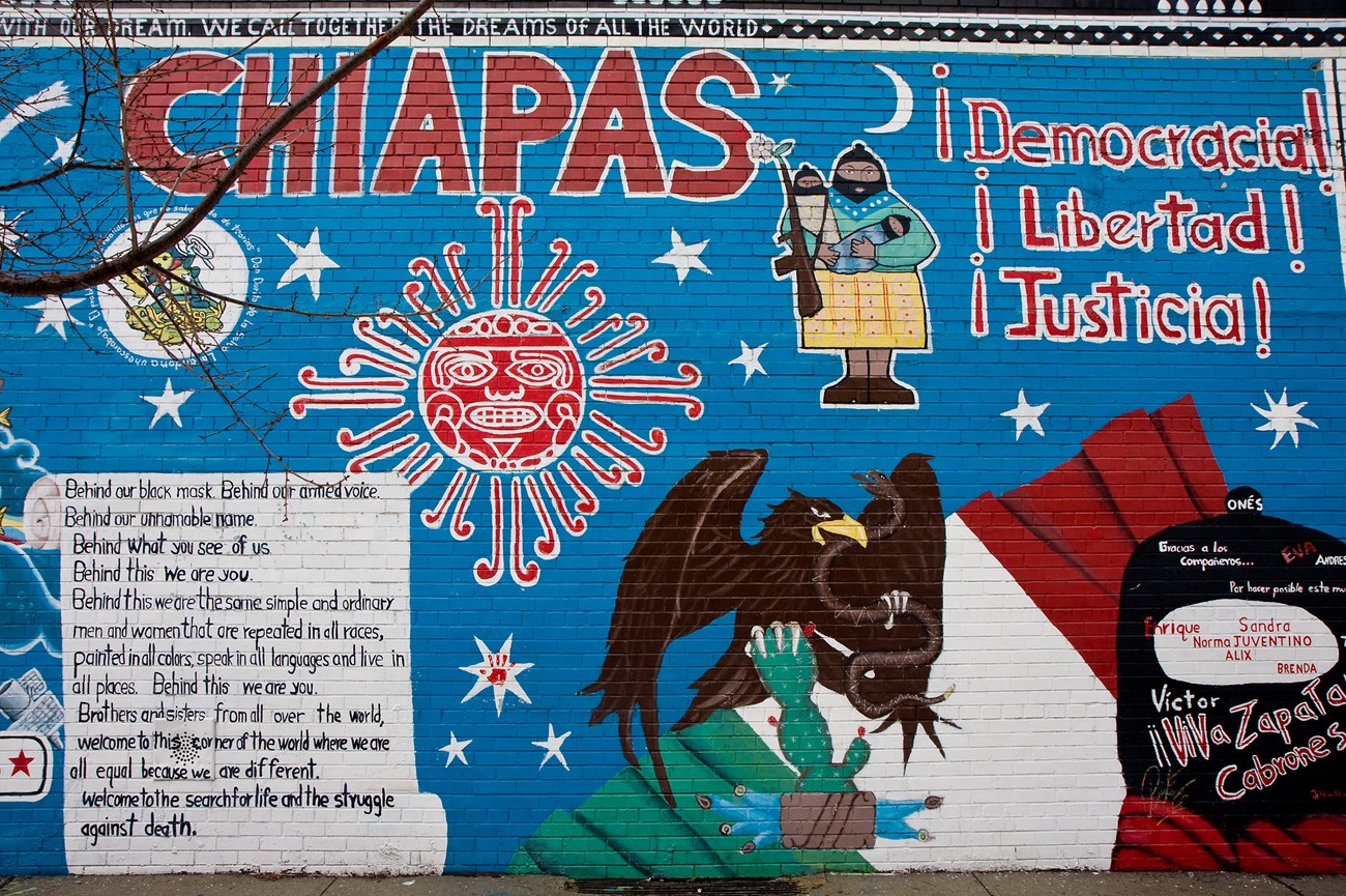 Zapatista mural, East Harlem Mural which Mexican and Mexican American iconography like the eagle with the snake, a rendering of the sun in the Aztec style, the terms “Libertad” and “Justicia,” and a poem on a blue background