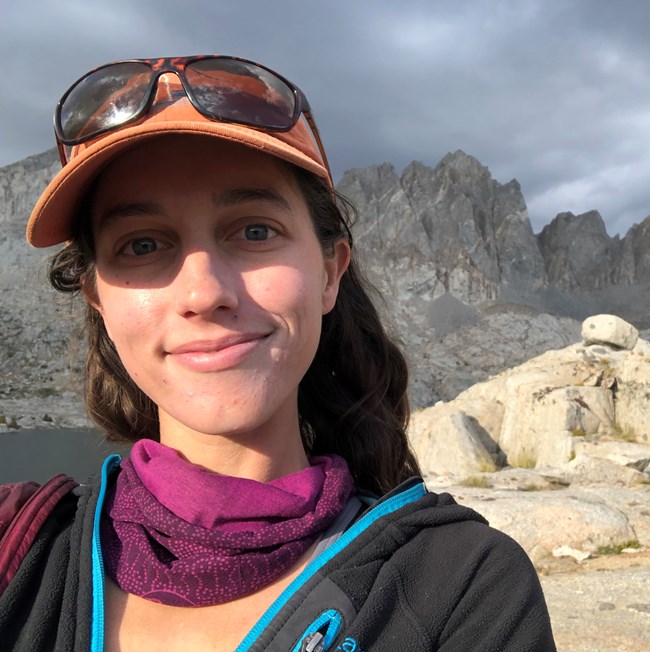 Smiling face of woman with high mountain spires in the background.