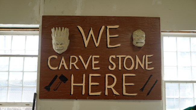A handpainted wooden sign that says "WE CARVE STONE HERE"
