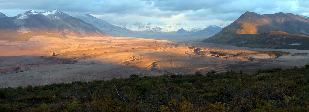 photo of a volcanic landscape with large flow deposit and snow covered peaks in the distance.