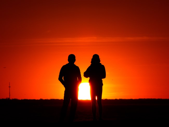 Two people in silhouette watching the sunset
