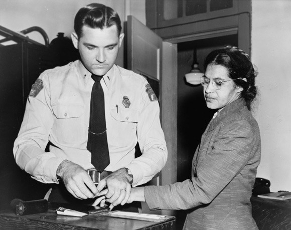 Rosa Parks stands while a white police officer fingerprints her.