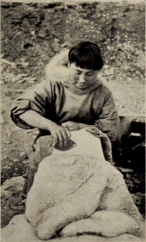 Ada Blackjack sits, scraping blubber from a sealskin with a curved blade called an ulu.