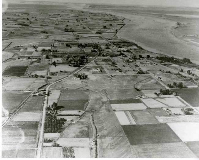 Aerial view of sparsely populated farming community with homes and fields along a wide river.