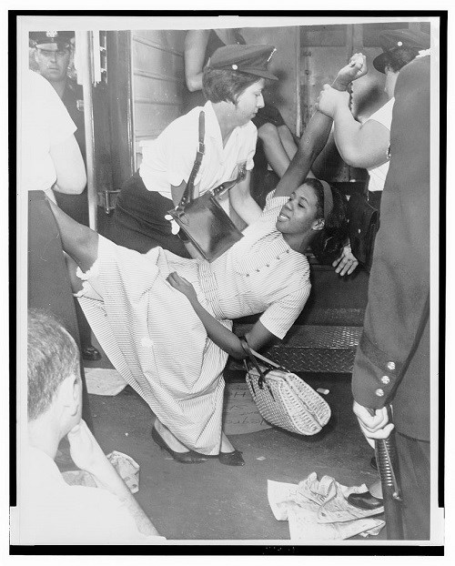 White policewomen carrying black woman wearing dress and carrying purse