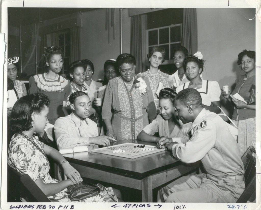 African American USO, early 1940s. Pictured is a group of people playing a board game on a table.