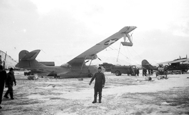 Plane with tie downs on, toppled by wind, and people nearby.