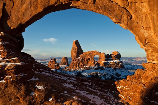 a rock arch frames another rock formation dusted with snow