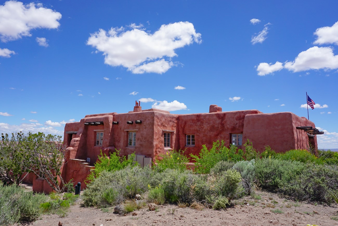 A red adobe building surrounded by green plants.