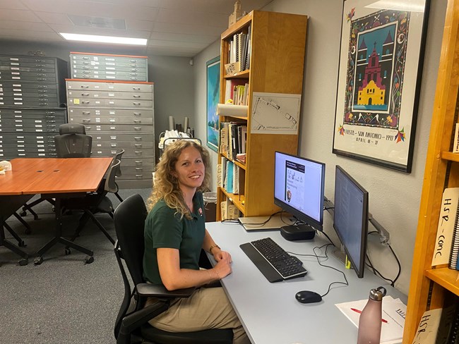 woman with blonde hair sitting on front of a computer looking at the camera