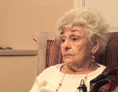 august_helen An older woman with glasses and grey, curly hair, sits in a chair.