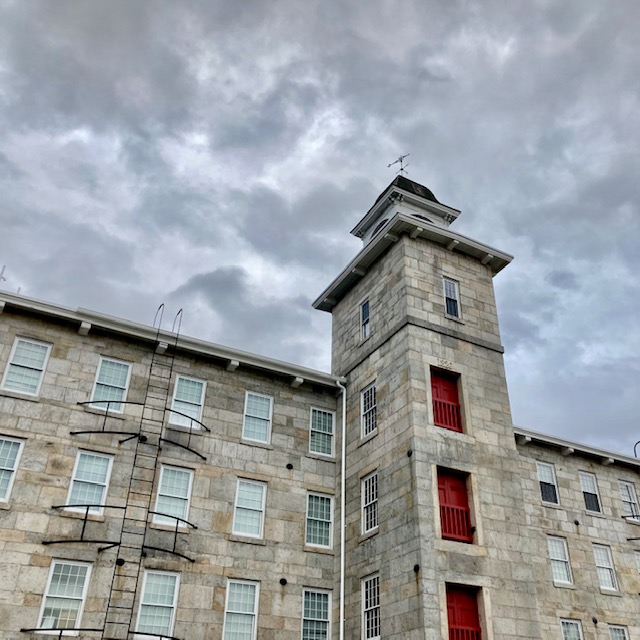 Slatersville Mill Grey stone mill with red trim and large central tower.