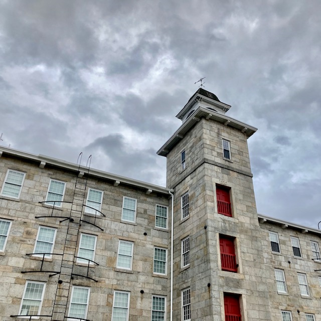 Grey stone mill with red trim and large central tower.