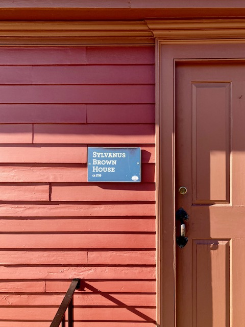 Sylvanus Brown House Close-up of facade of red colonial wooden clapboard house with plaque that reads "Sylvanus Brown House, circa 1758