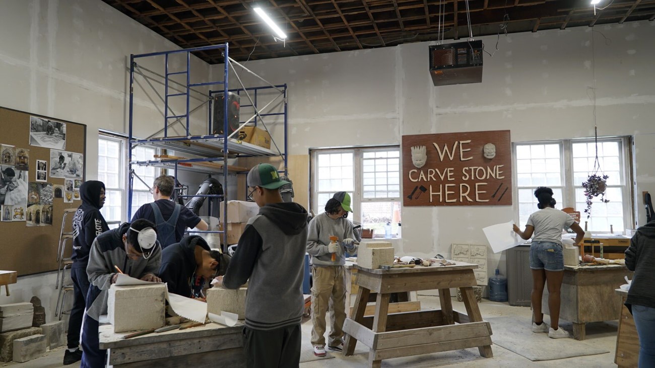 Classroom in action Students stand at work tables and carve large blocks of stone