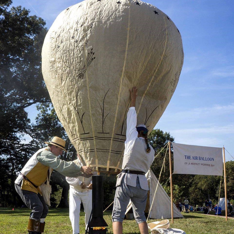 A large balloon held by three men while it fills.