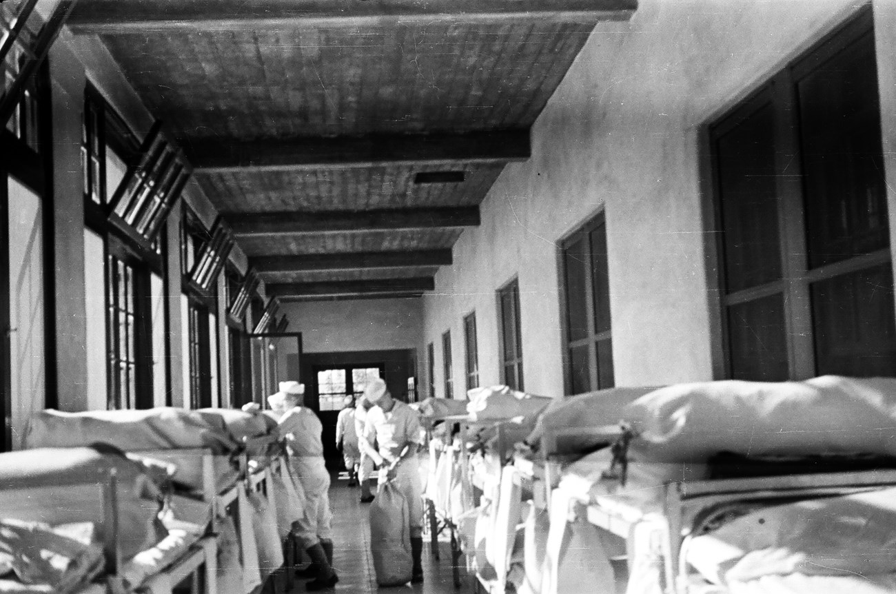 Barracks elevated bed with men in uniform and white cloth bags