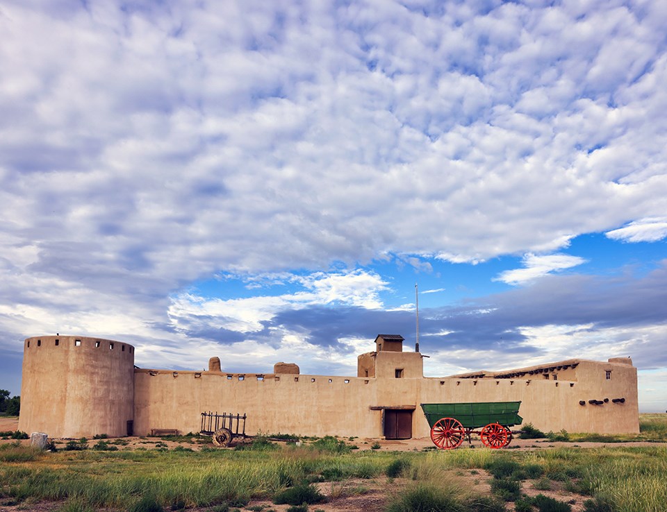Bent's Old Fort National Historic Site An old fort and a couple of old wagons under a cloud-filled sky.