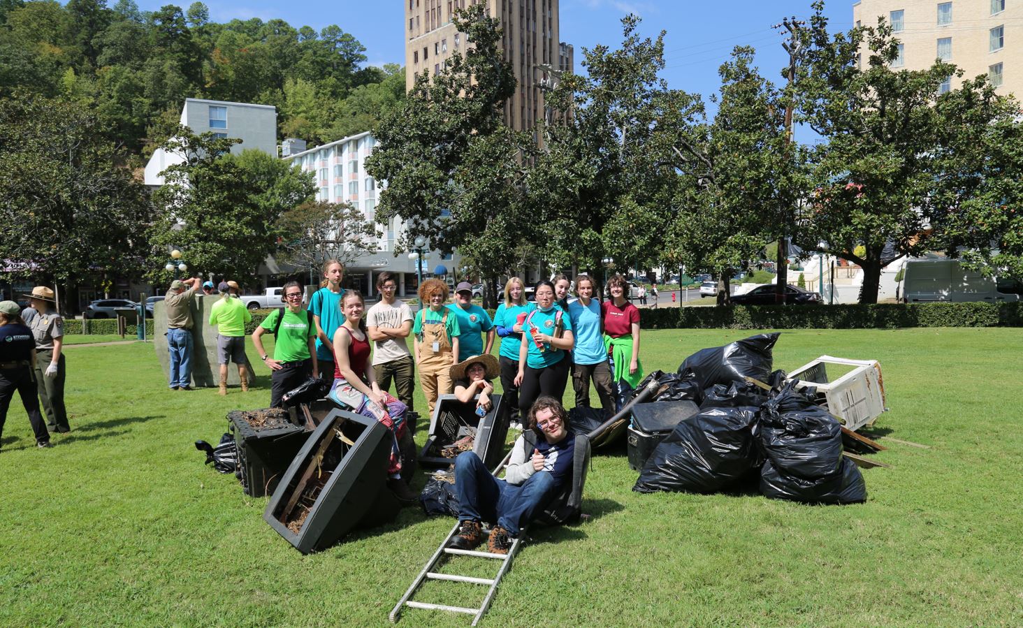 A large group of volunteers pose and gather around a large pile of trash collected