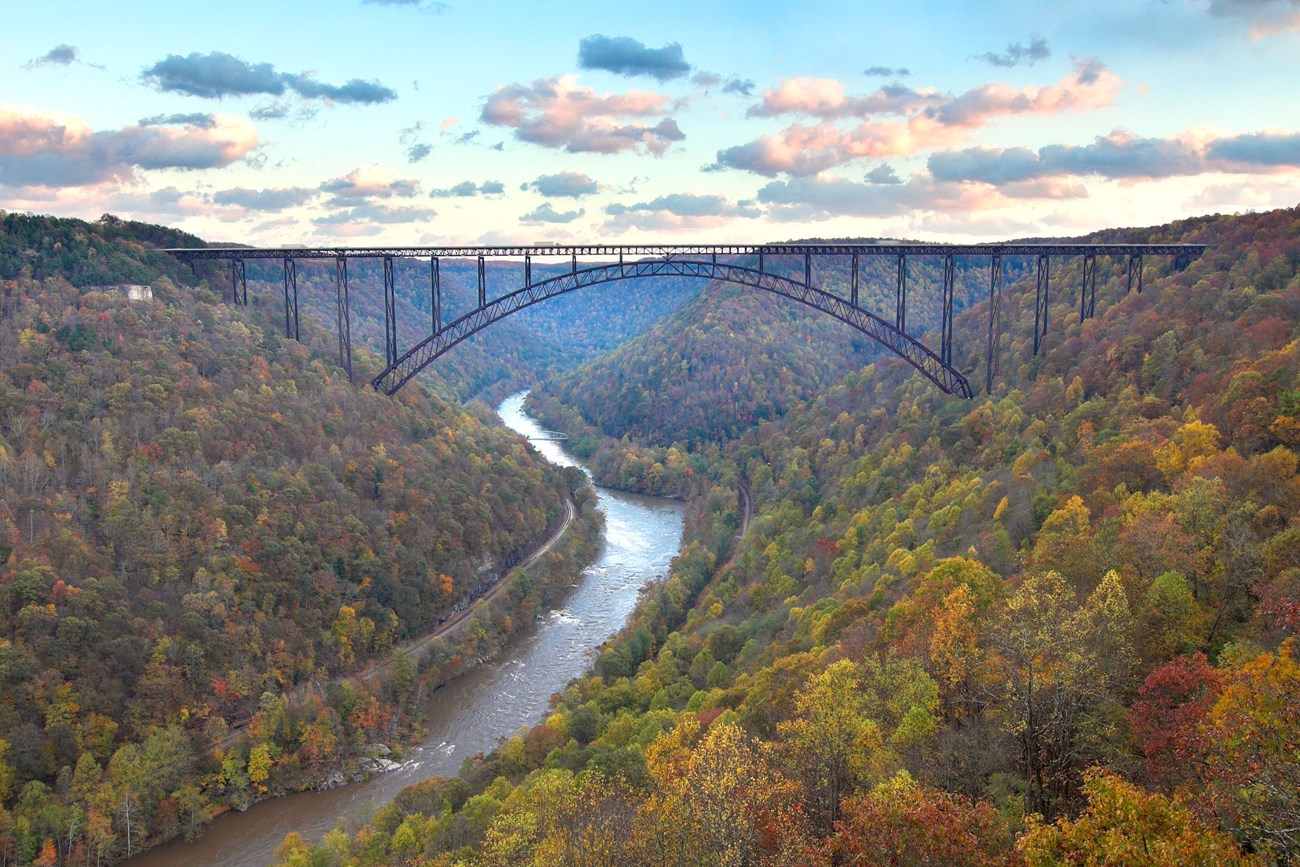 New River Gorge National Park and Preserve An aerial view of a river running through two hills filled with colorful trees and a bridge connecting them.
