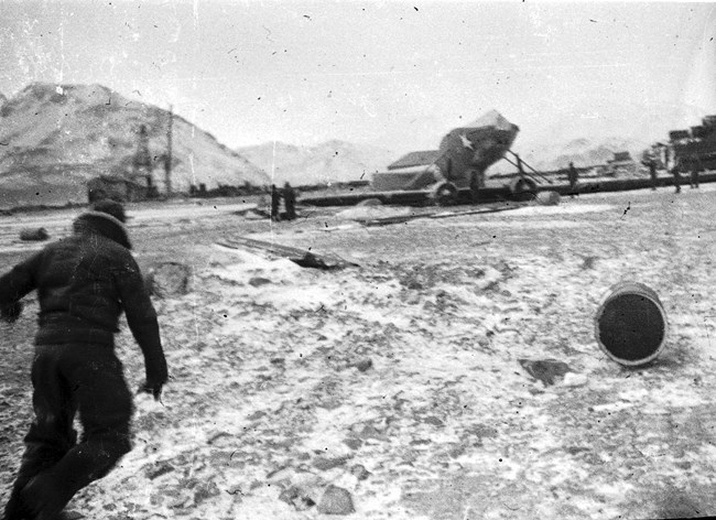 Man in cold weather gear runs towards an upside-down plane on a runway.