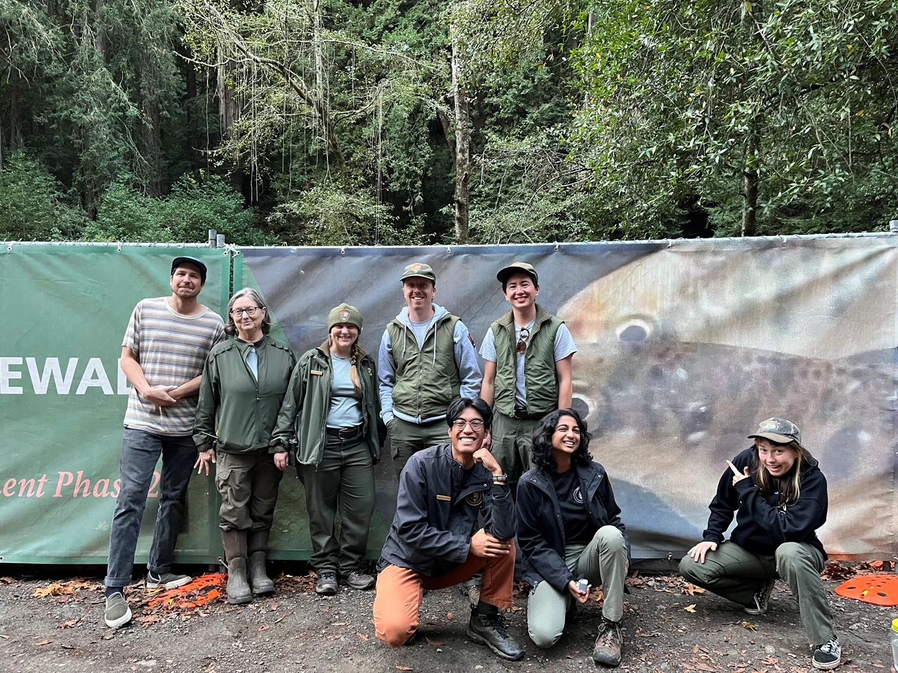 Biomonitors Eight park staff and interns gather for a photo in front of a banner Muir Woods featuring a photo of juvenile coho salmon.