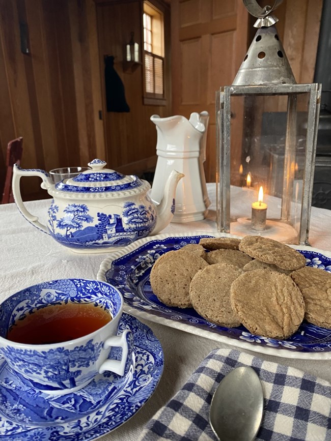 A plate of cookies next to a candle lantern and a cup of tea.