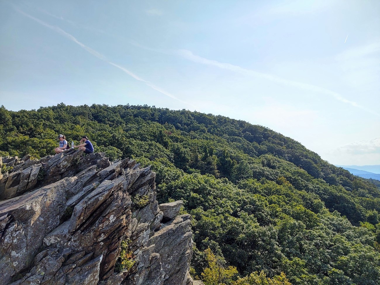 Humpback Rocks Two hikers sitting on large rocks at a scenic viewpoint with rolling hills in the distance.