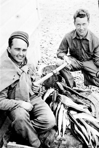 Two smiling men crouched by pile of fish.