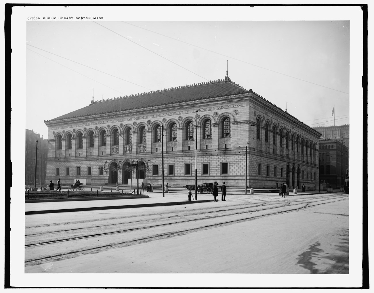 A black and white photo of a high style building. It has ornate details along the roof and is lined with large windows across the facade. Stone details emphasize the high level of ornamentation on the entire building.