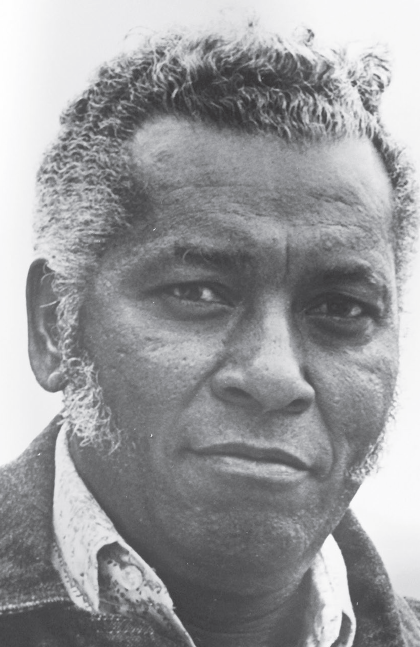 a historic scene of a Black man with graying hair and long sideburns with a subtle smile.