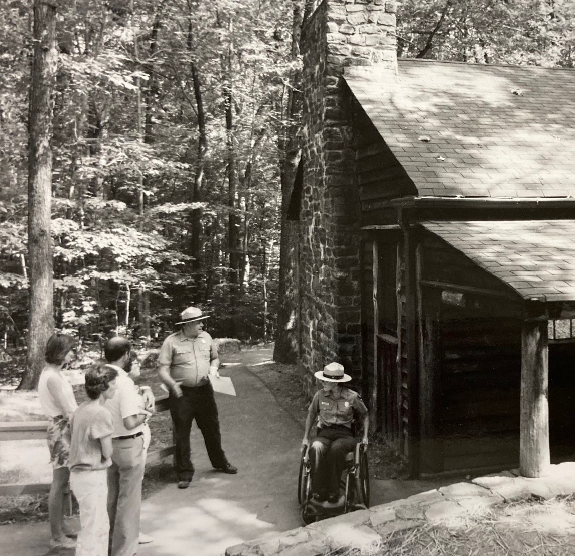 Erin Broadbent at Prince William Forest Erin Broadbent in a wheelchair and a male ranger with visitors outside a cabin.