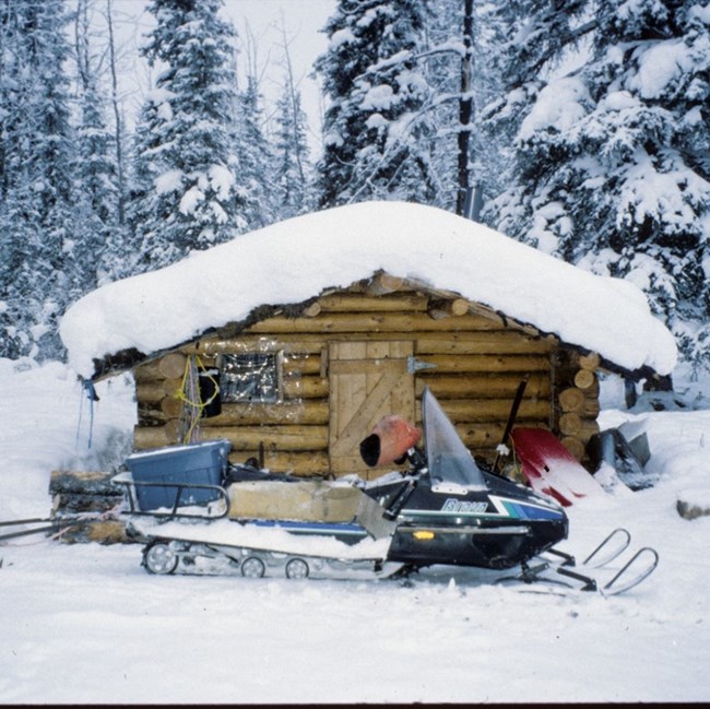 A log cabin in the snow with a snowmachine in front.